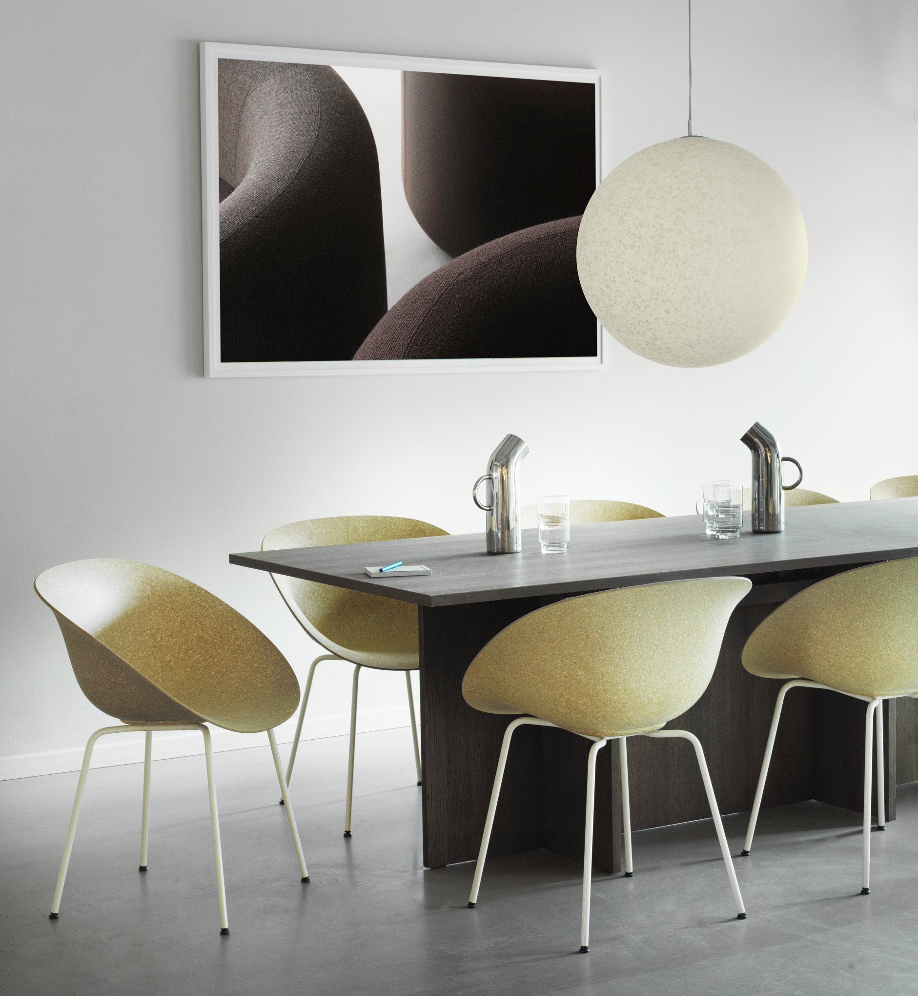 Seven sustainable armchairs made with hemp, at a long office table with a round celing light and modern artwork on the wall.