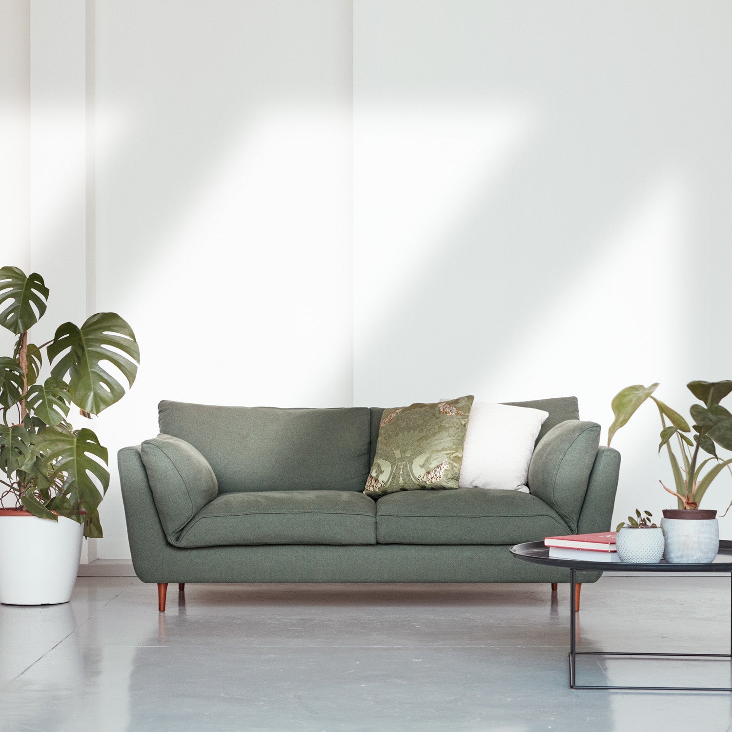 A sustainable two-seater sofa made with natural latex cushions by Biosofa is shown in a living room with potted plants.