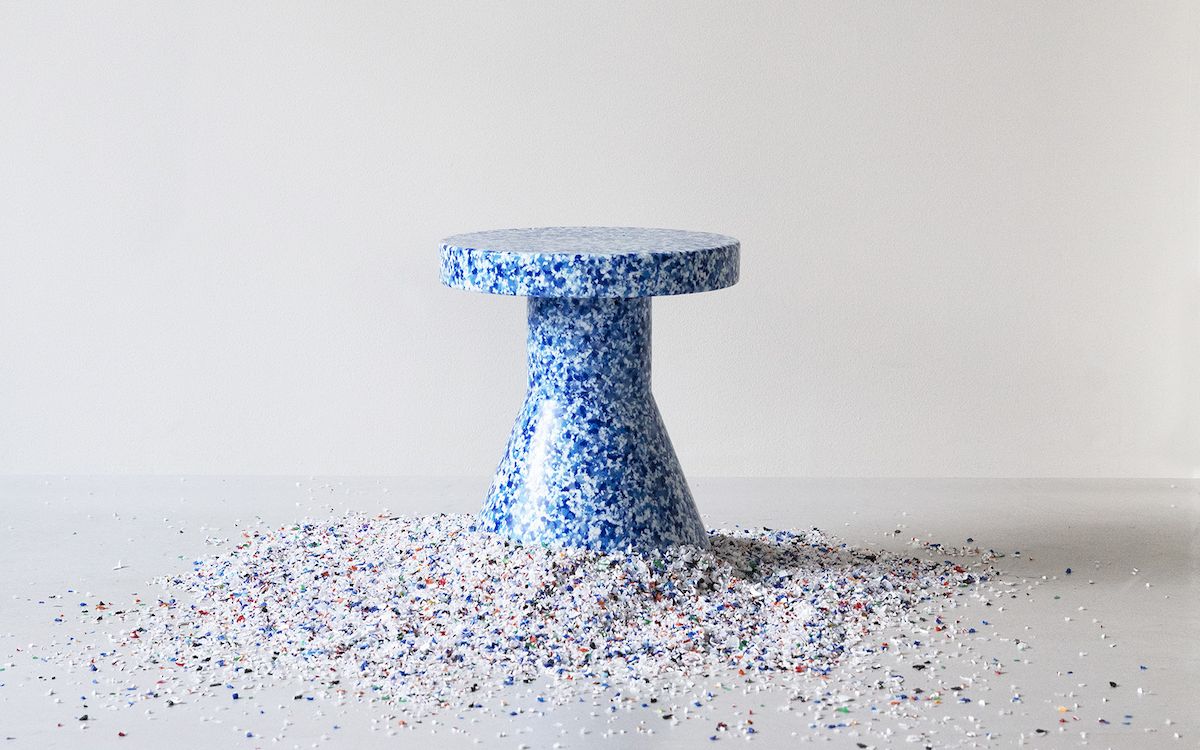 A Bit Stool Cone in Blue, by Normann Copenhagen, with a pile of recycled plastic pellets used to make it.