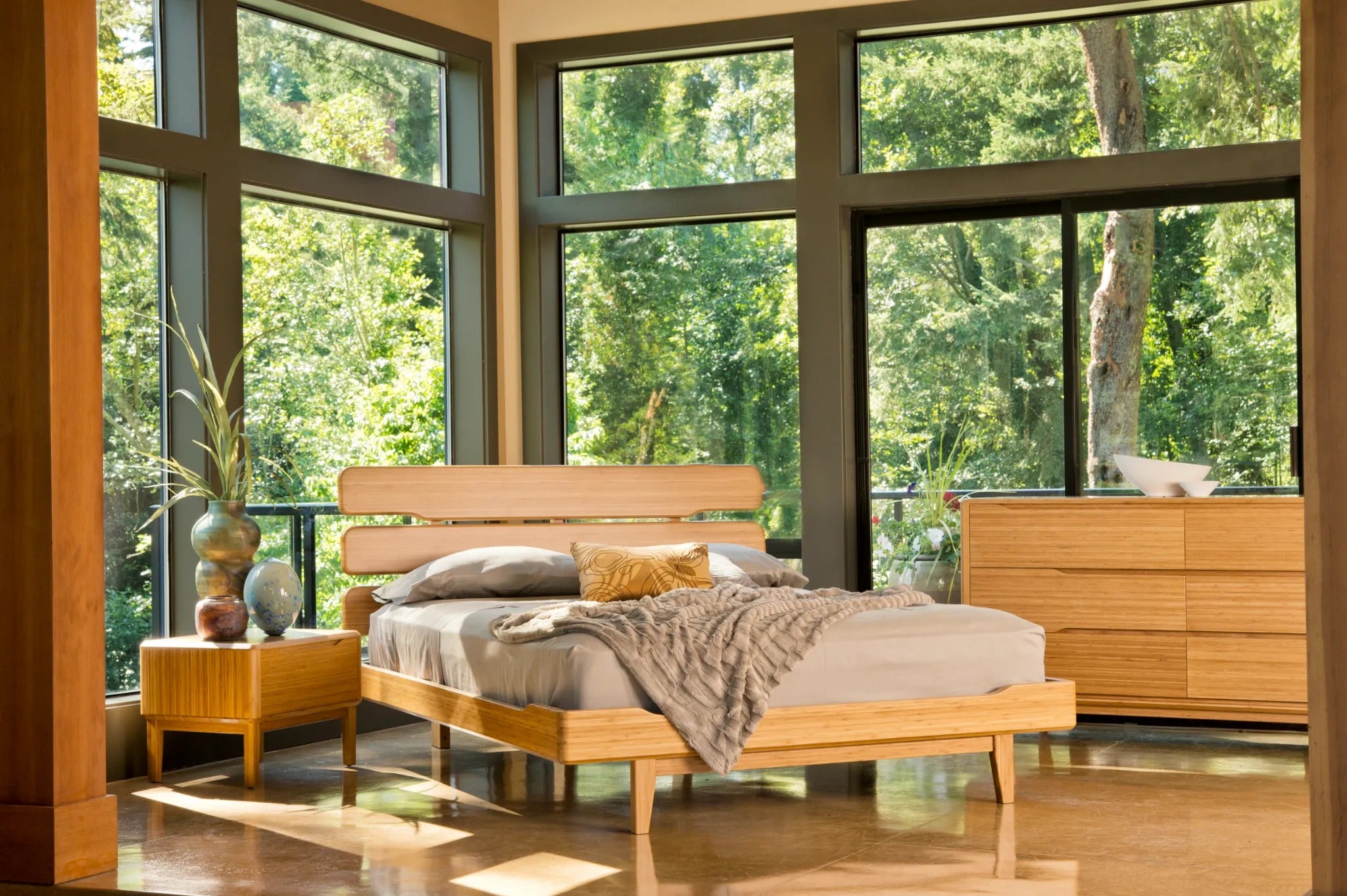 A renewable Currant Bamboo Bedframe by Greenington, in caramel color, placed in a bedroom with a low dresser and a nightstand next to it.