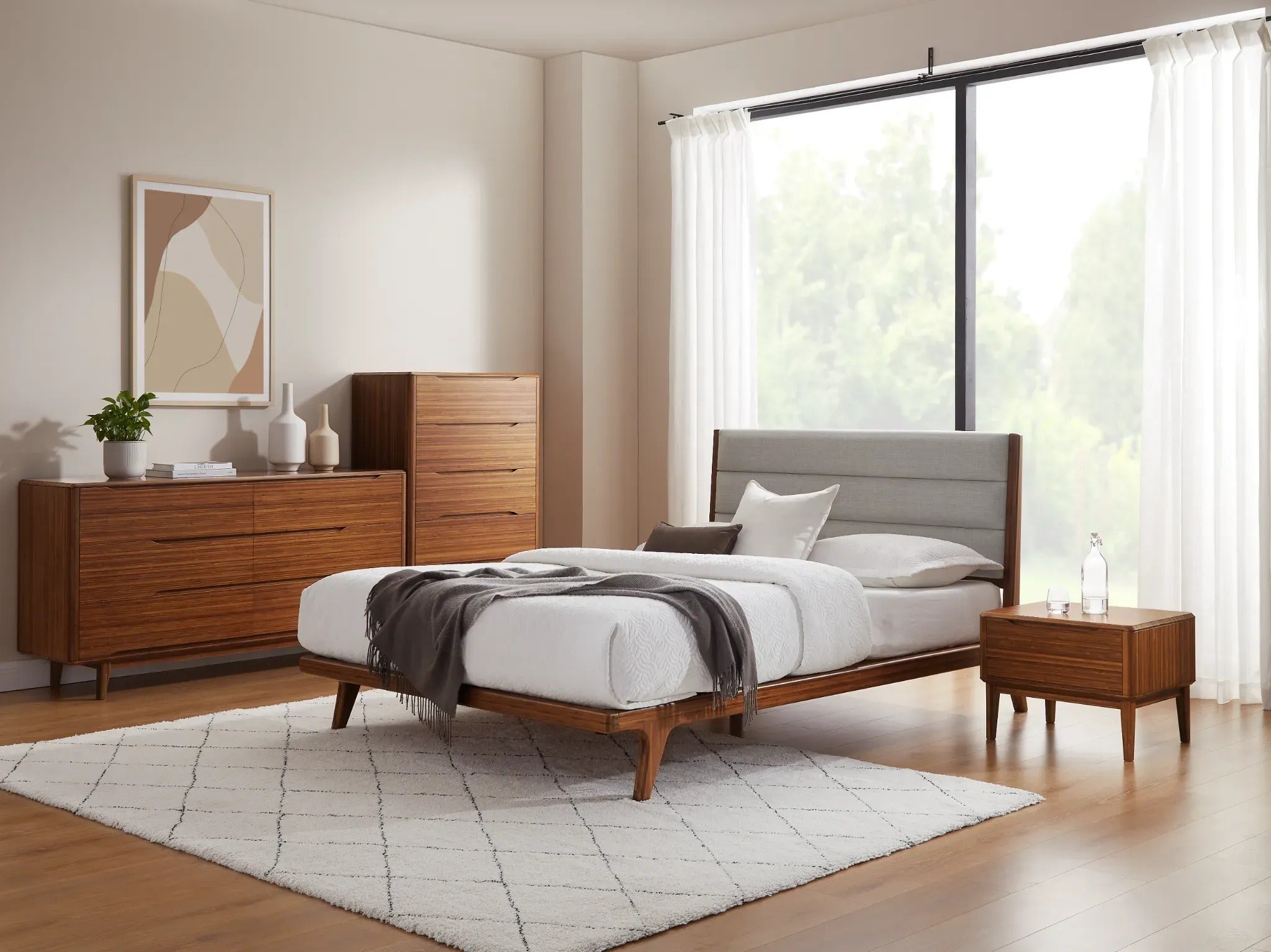 A renewable Currant Bamboo Low Dresser by Greenington, in amber color, placed in a bedroom alongside the bed, a high dresser, and a nightstand.