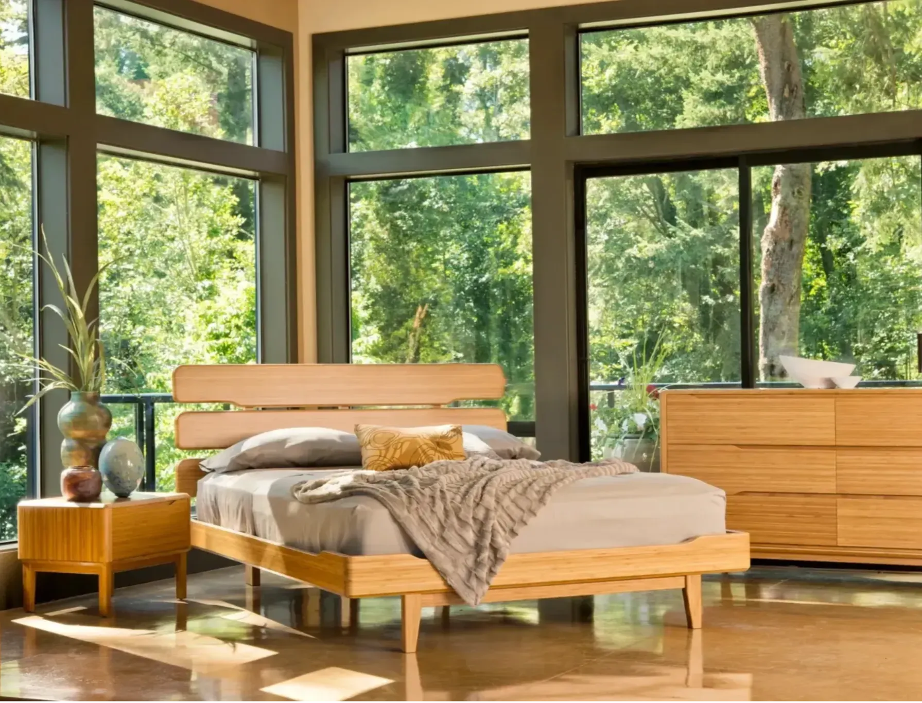 A bamboo sustainable bed with a bamboo dresser and nightstand, in a bright, sunny bedroom with trees outside.