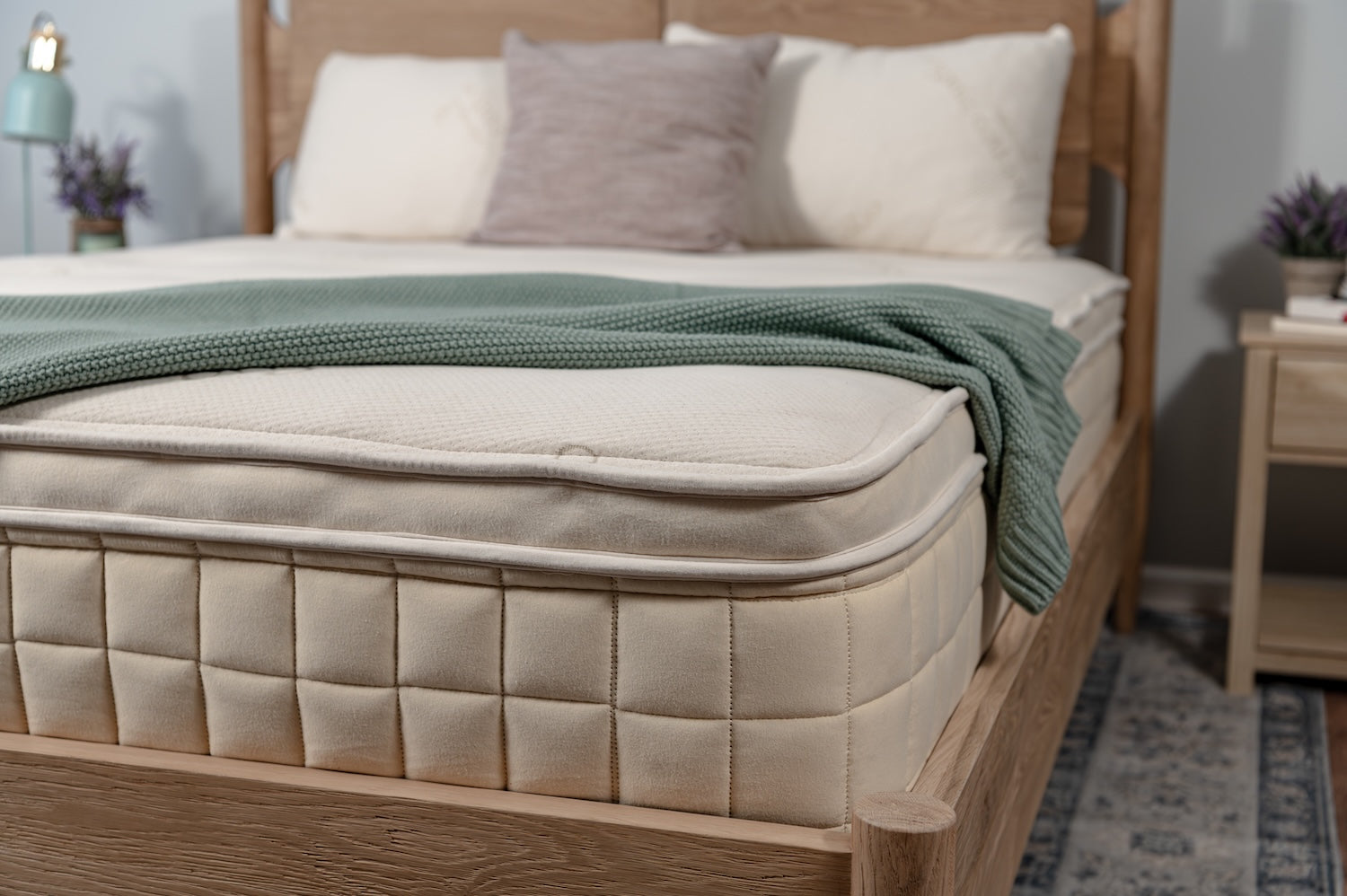 Bed with wooden frame, beige mattress, and green blanket in a bedroom setting.