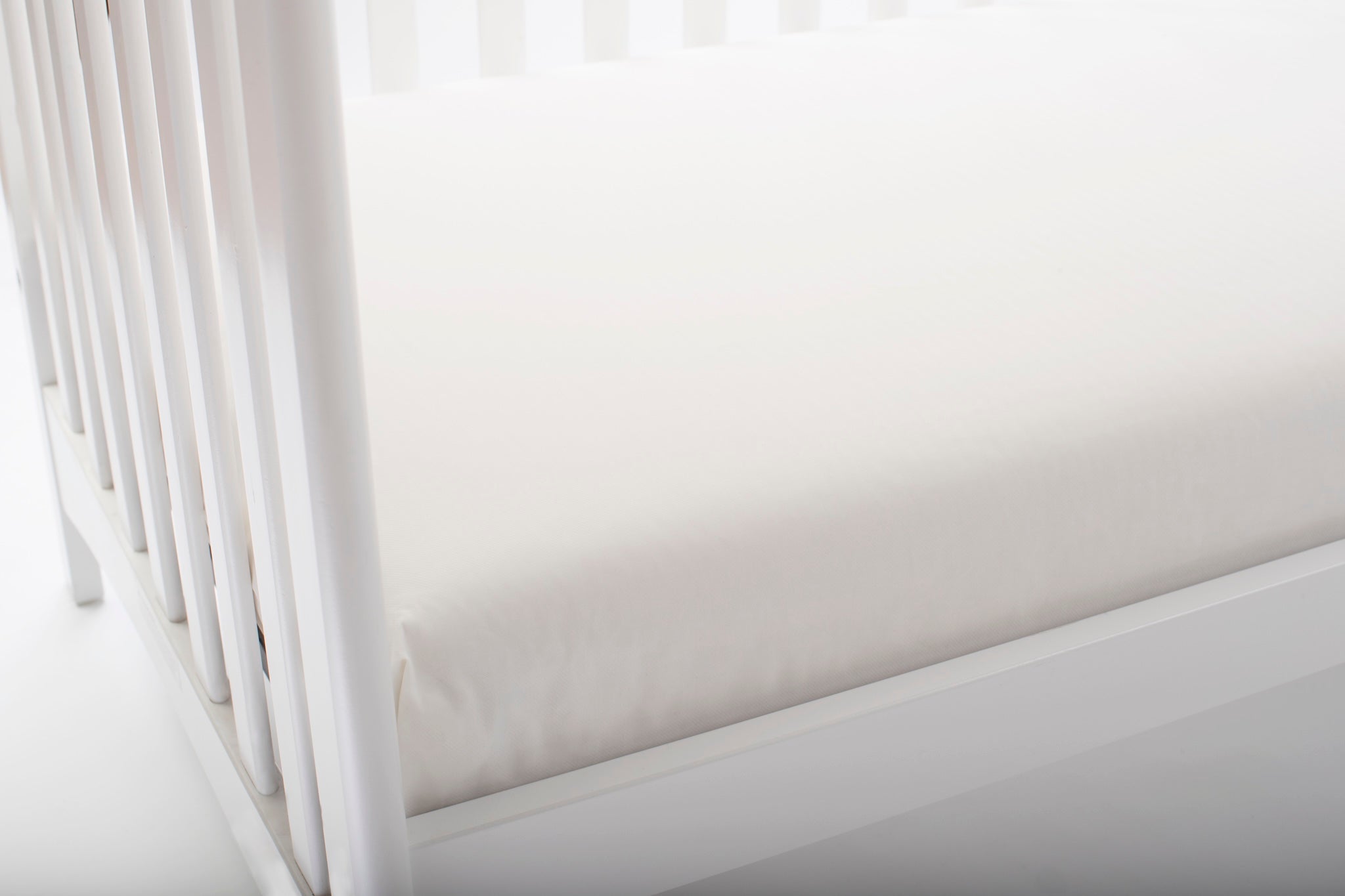 White crib with a fitted sheet on a white background