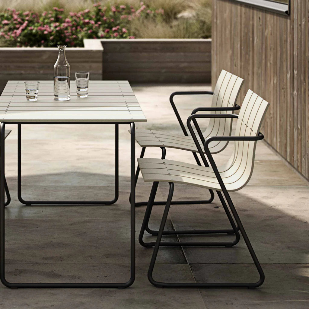 An Ocean Table made with recycled materials by Mater, in sand color, with two matching chairs on a beachfront wood deck.