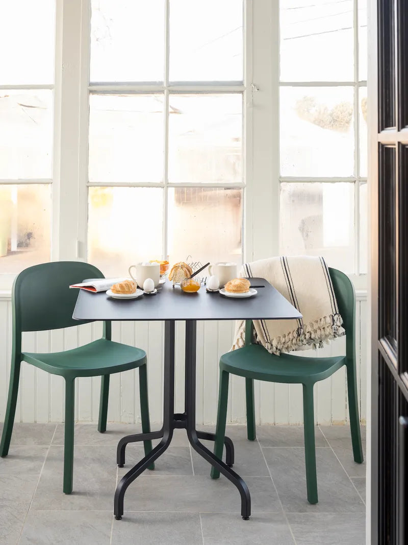 A sustainable table with two recycled plastic Reclaimed Chairs by Emeco, in green.