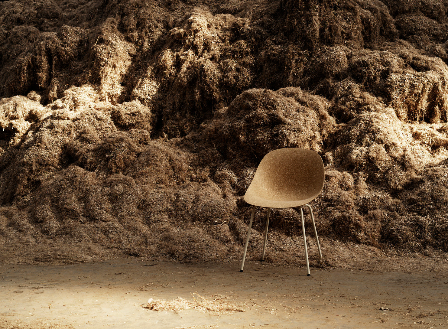 A eco-friendly chair made with hemp plants, by Normann Copenhagen, sitting in a large pile of shredded hemp plants used to make it.