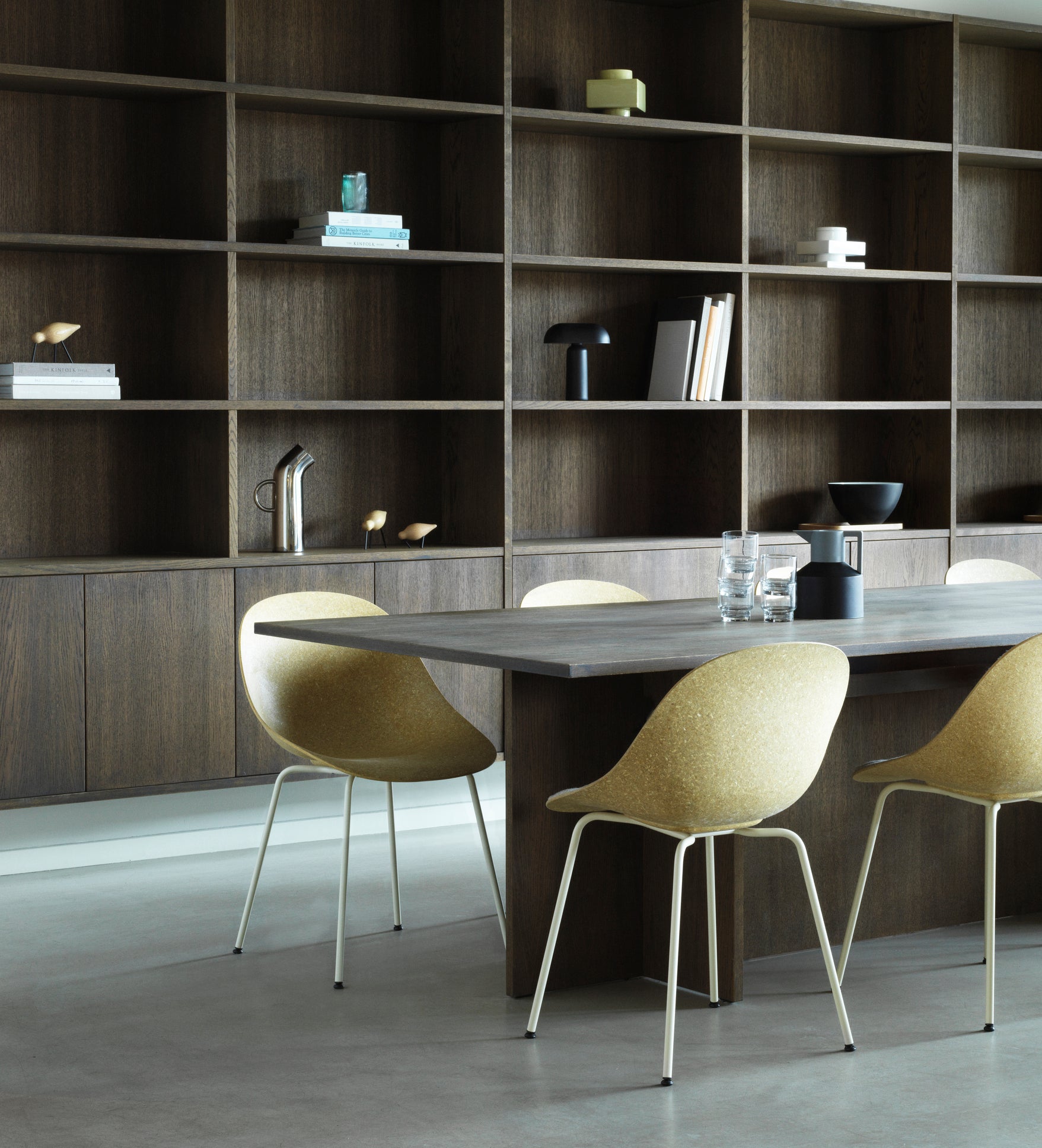 Six hemp chairs by Normann Copenhagen, with white-coated legs, around a grey rectangluar office table with a wood wall unit background.