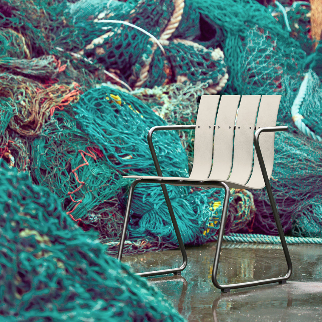 A sustainable outdoor chair by Mater, surrounded by discarded green fishing nets waiting to be recycled into the Ocean Chair shown here.