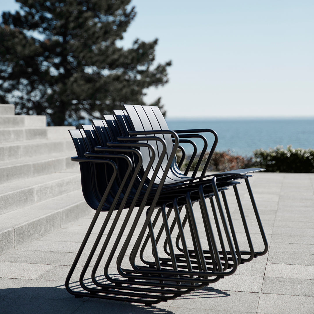 A stack of six Ocean Chairs made of recycled plastic by Mater, in black, in a sunny outdoor courtyard.