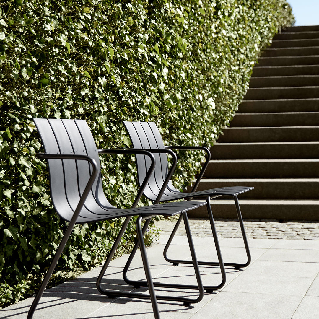 Two Ocean Chairs made of recycled material by Mater, in black, in front of an ivy covered wall and stone stairs.