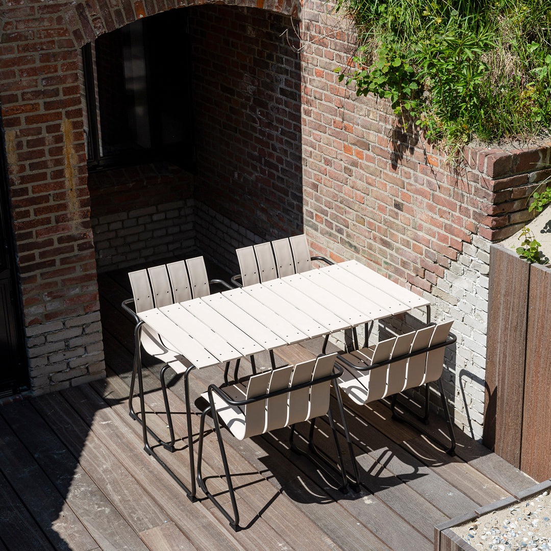 Four white Ocean Chairs and a matching rectangular table in a outdoor courtyard, made of recycled plastic and metal.