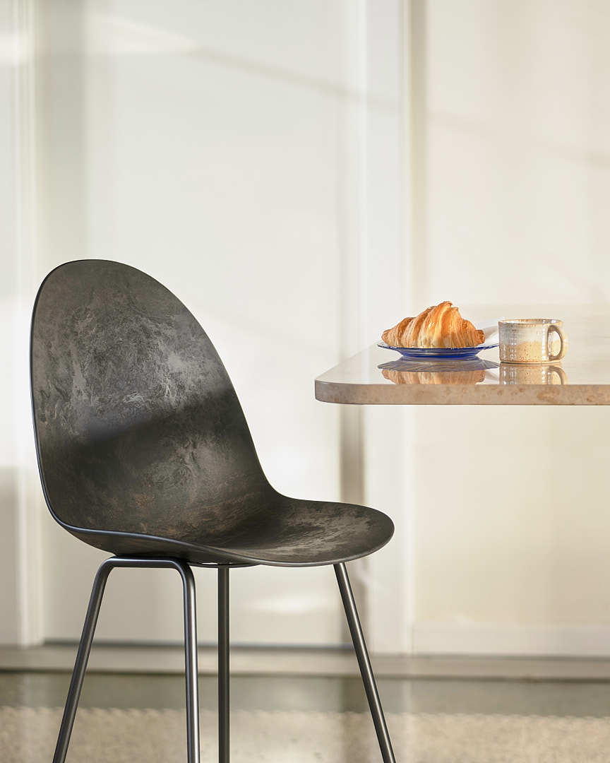 A sustainable dark Matek eternity chair made with recycled material by Mater, next to a single dining table.