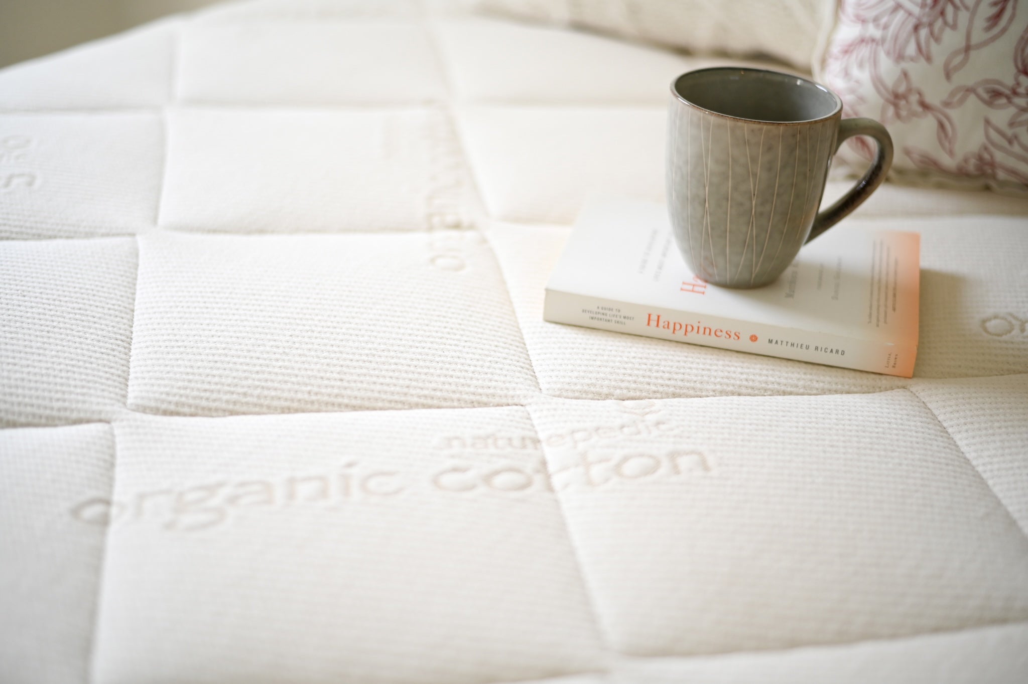 Mattress with 'organic cotton' branding, a mug, and a book on top