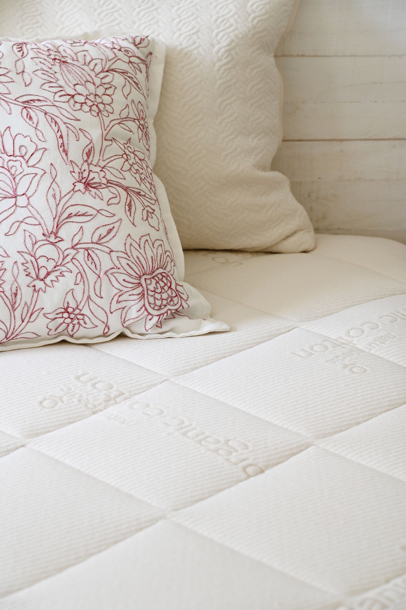 Close-up of a white quilted mattress with decorative pillows on a bed.