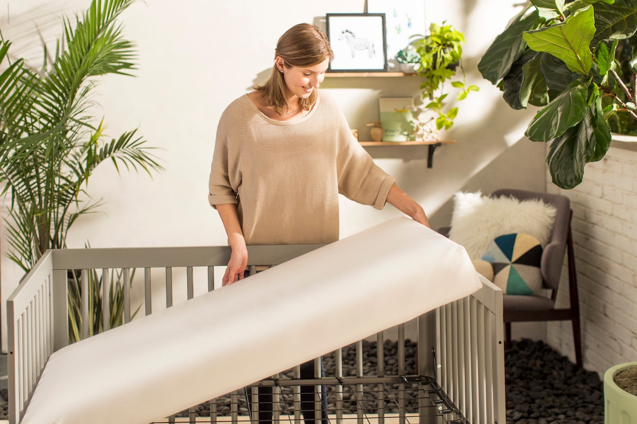 Woman setting up a crib in a room with plants and furniture.