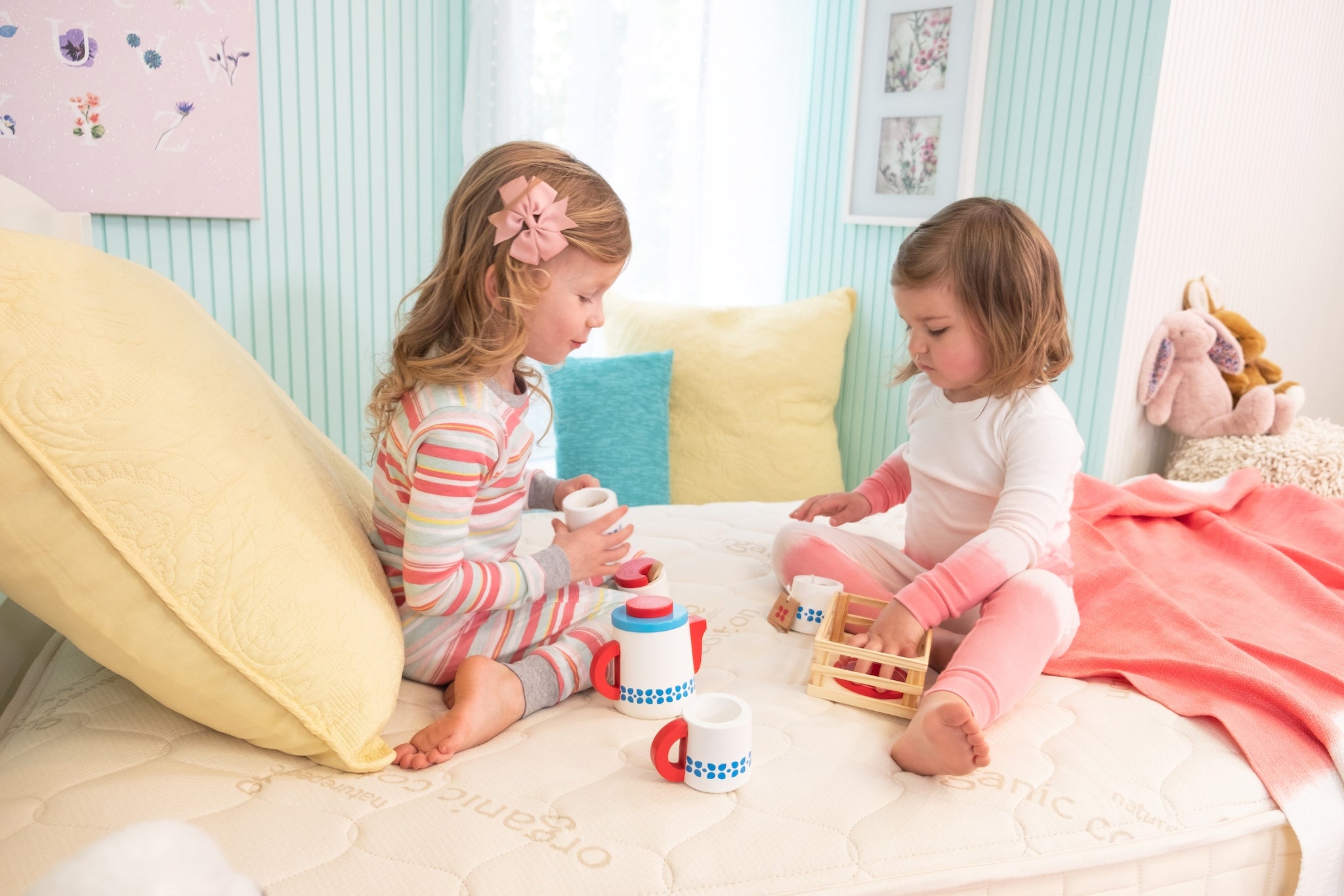 Two young girls playing with toys on a bed in a child-friendly room.